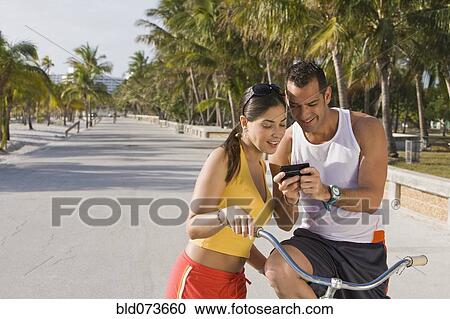 Stock Image - Hispanic couple on bicycles looking at cell phone. Fotosearch