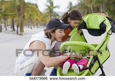 Stock Photograph - Hispanic father and daughter checking on baby in stroller. Fotosearch