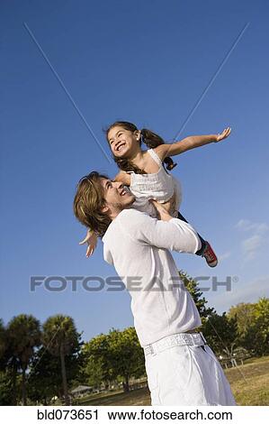 Stock Image - Hispanic father lifting daughter into the air. Fotosearch