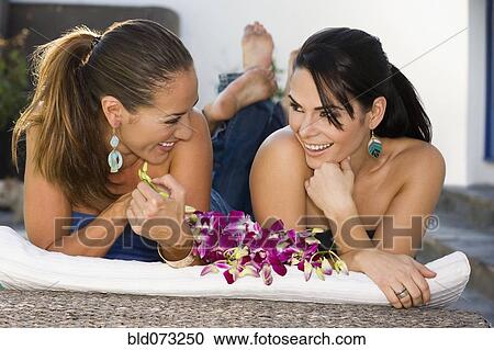 Stock Image - Hispanic friends laying outdoors talking. Fotosearch