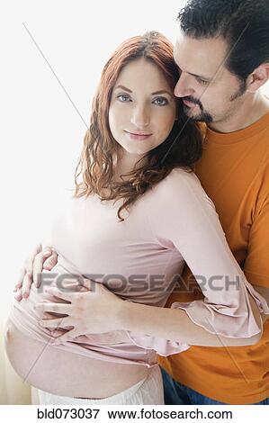 Stock Photo - Hispanic man hugging pregnant wife. Fotosearch
