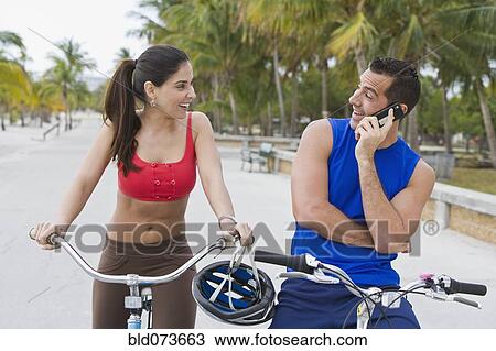 Hispanic man on bicycle talking on cell phone while girlfriend waits View Large Photo Image Stock Image - Hispanic man on bicycle talking on cell phone while girlfriend waits. Fotosearch