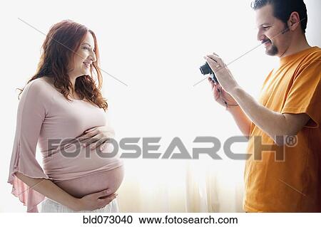 Stock Image - Hispanic man taking photograph of pregnant wife. Fotosearch