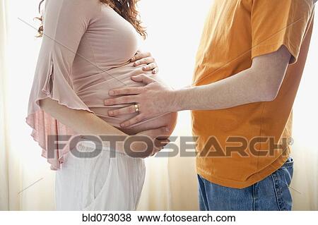 Stock Photo - Hispanic man touching pregnant wife’s stomach. Fotosearch
