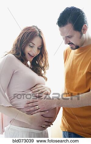 Stock Photo - Hispanic man touching pregnant wife’s stomach. Fotosearch