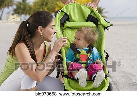 Stock Photo - Hispanic woman checking on baby in jogging stroller. Fotosearch