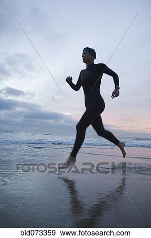 Hispanic woman in wetsuit running on beach View Large Photo Image Stock Photo - Hispanic woman in wetsuit running on beach. Fotosearch