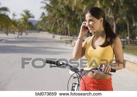 Hispanic woman on bicycle talking on cell phone View Large Photo Image Stock Photo - Hispanic woman on bicycle talking on cell phone. Fotosearch