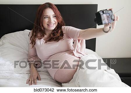 Stock Image - Hispanic woman taking self-portrait of pregnant stomach. Fotosearch