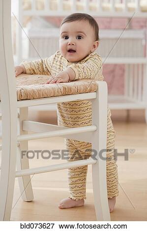 Stock Photo - Mixed race baby girl balancing near chair. Fotosearch