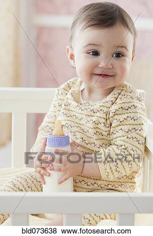 Stock Photo - Mixed race baby girl holding bottle. Fotosearch