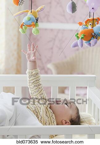 Stock Photography - Mixed race baby girl reaching for toy mobile. Fotosearch