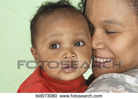 Stock Image - Mixed race mother holding baby daughter. Fotosearch