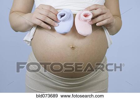 Stock Photo - Pregnant Chinese woman holding pink and blue booties. Fotosearch