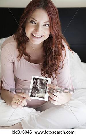 Stock Photograph - Pregnant Hispanic woman holding sonogram picture. Fotosearch