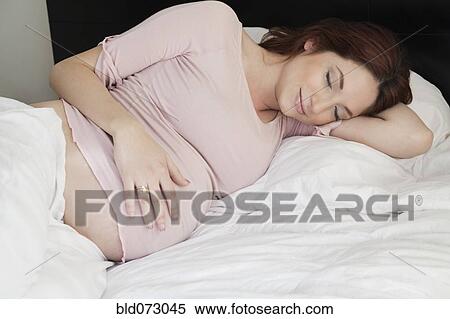 Stock Photography - Pregnant Hispanic woman napping in bed. Fotosearch