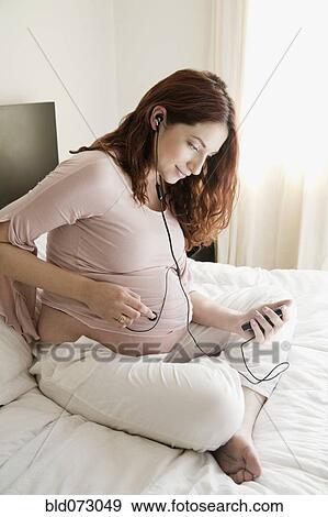 Stock Photo - Pregnant Hispanic woman playing music for unborn baby. Fotosearch
