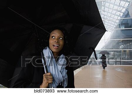 Stock Image - African businesswoman holding umbrella in rain. Fotosearch