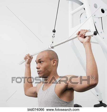 Stock Photograph - African man using weight machine in health club. Fotosearch
