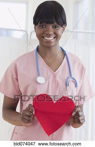 Stock Photo - African nurse holding heart-shaped piece of paper. Fotosearch