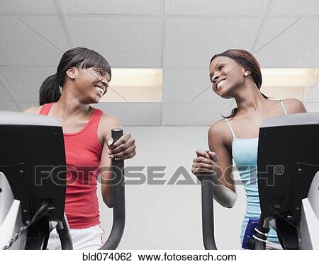 Stock Image - African women using exercise equipment in health club. Fotosearch