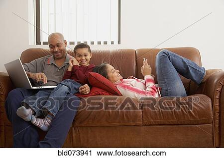 Stock Image - Antiguan man using laptop in living room with family. Fotosearch