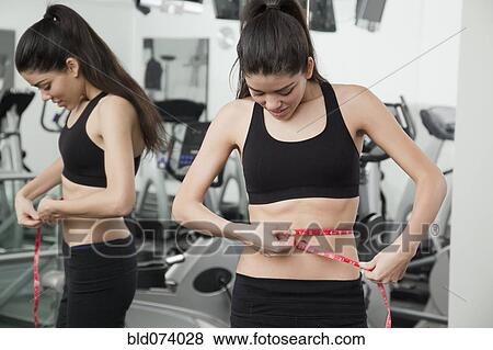 Hispanic woman checking waist measurement in health club View Large Photo Image Stock Photo - Hispanic woman checking waist measurement in health club. Fotosearch