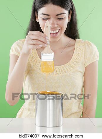 Stock Photo - Hispanic woman holding paintbrush over paint can. Fotosearch