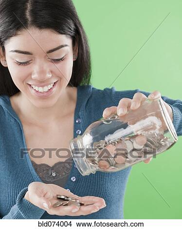 Picture - Hispanic woman pouring coins out of jar. Fotosearch