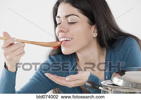 Stock Image - Hispanic woman tasting tomato sauce. Fotosearch