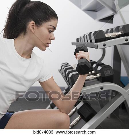 Stock Image - Hispanic woman using hand weights in health club. Fotosearch