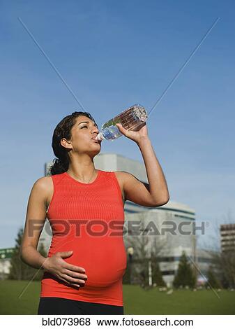 Stock Photo - Pregnant Middle Eastern woman drinking water outdoors. Fotosearch