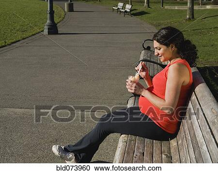 Stock Image - Pregnant Middle Eastern woman eating fruit in park. Fotosearch