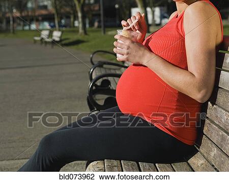 Stock Image - Pregnant Middle Eastern woman eating fruit in park. Fotosearch