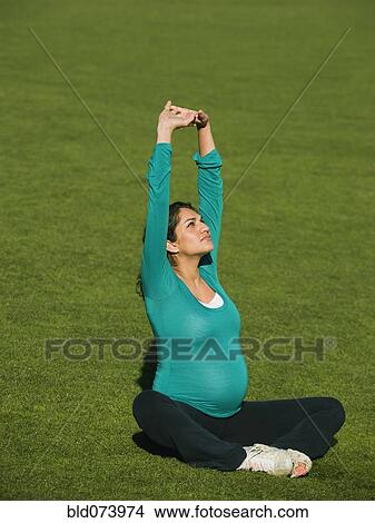 Picture - Pregnant Middle Eastern woman practicing yoga in park. Fotosearch