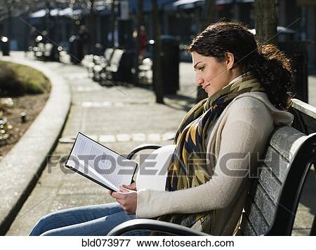 Stock Photo - Pregnant Middle Eastern woman reading on park bench. Fotosearch
