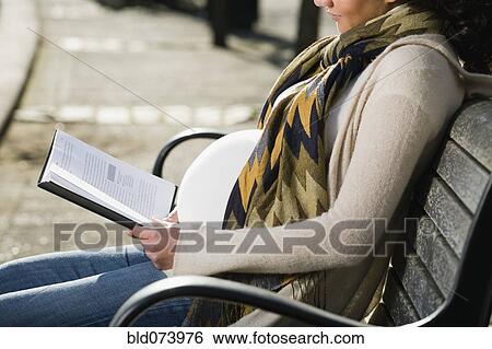 Stock Photograph - Pregnant Middle Eastern woman reading on park bench. Fotosearch