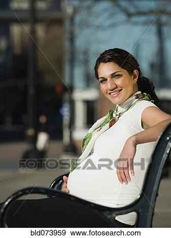 Stock Photo - Pregnant Middle Eastern woman sitting on park bench. Fotosearch