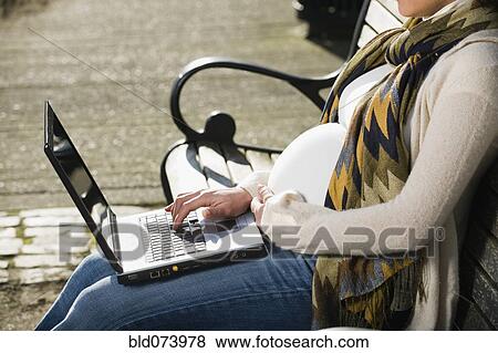 Stock Photo - Pregnant Middle Eastern woman using laptop on park bench. Fotosearch
