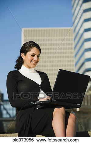 Stock Photograph - Pregnant Middle Eastern woman using laptop outdoors. Fotosearch