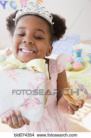 Picture - African girl eating cupcake and carrying gift. Fotosearch