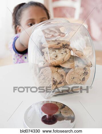Stock Image - African girl taking cookie from jar. Fotosearch