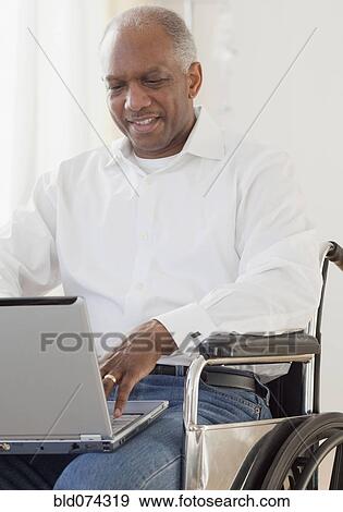 Stock Photo - African man in wheelchair using laptop. Fotosearch