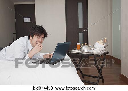 Stock Image - Asian businessman working in hotel room. Fotosearch
