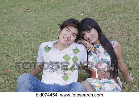 Picture - Asian couple sitting in grass together. Fotosearch