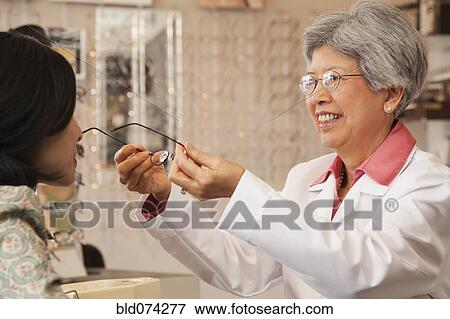 Stock Photo - Chinese optician fitting eyeglasses on customer. Fotosearch