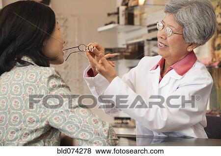 Stock Photo - Chinese optician fitting eyeglasses on customer. Fotosearch