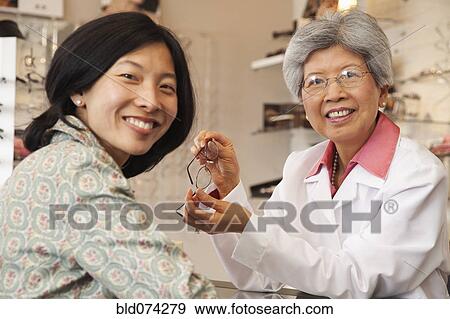 Stock Photo - Chinese optician fitting eyeglasses on customer. Fotosearch