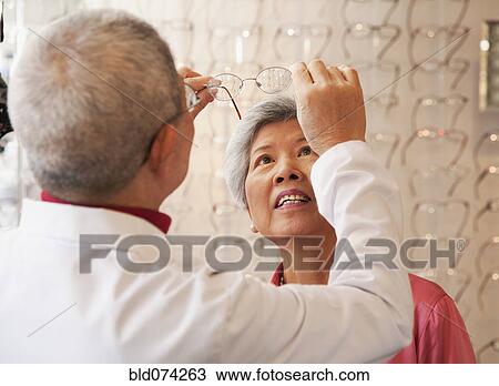 Stock Image - Chinese optician fitting woman's eyeglasses. Fotosearch