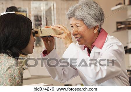 Stock Photograph - Chinese optician giving customer eye exam. Fotosearch